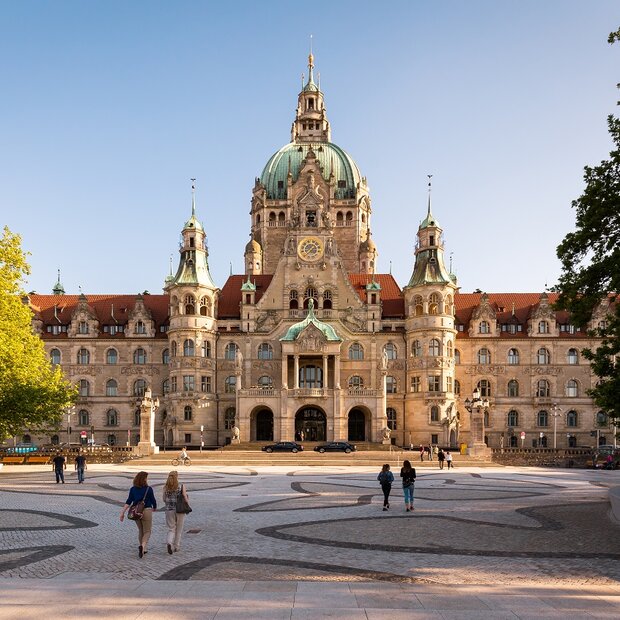 Außenansicht des Neuen Rathauses mit grünen Bäumen unter blauem Himmel.