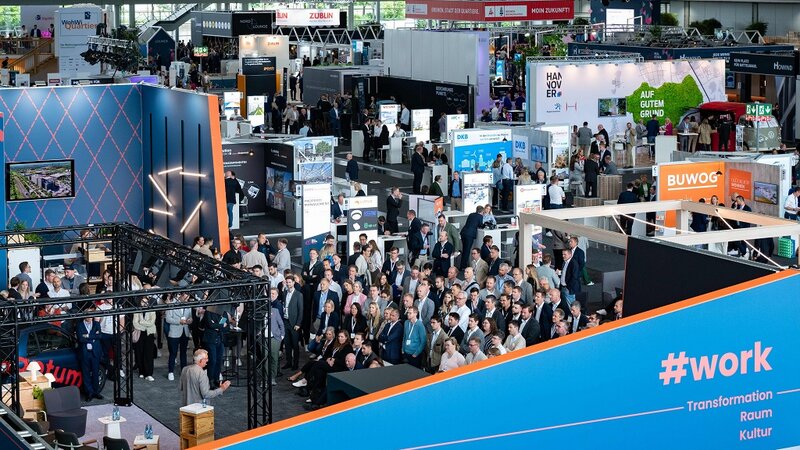 Innenansicht einer Messehalle mit Besucherinnen und Besuchern aus erhöhter Position.