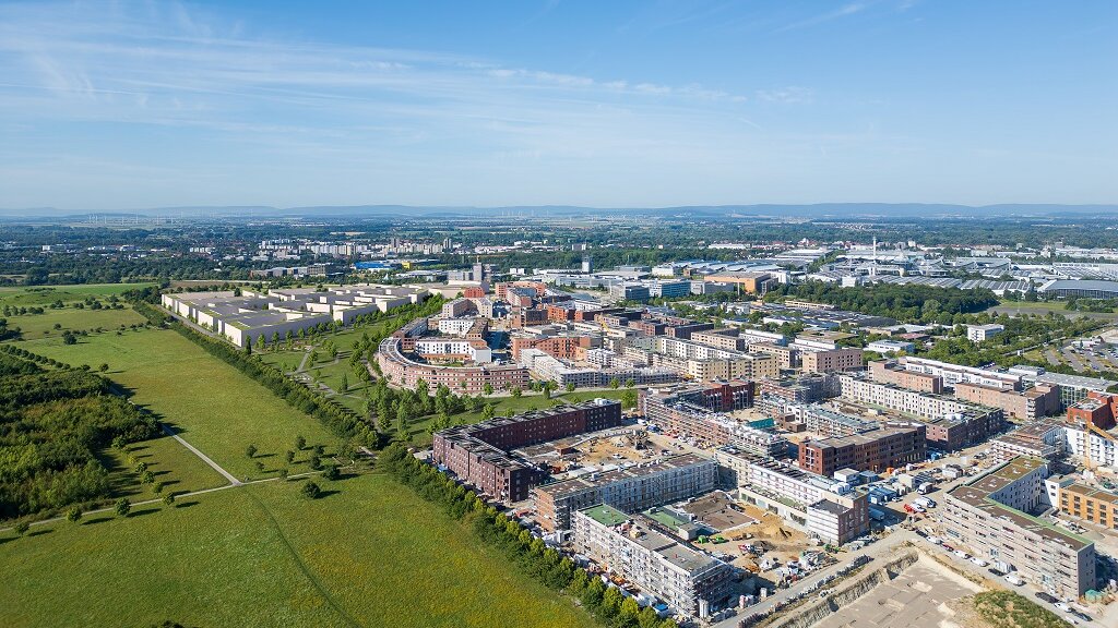 Ein Luftbild einer Wohnsiedlung mit Wohnblöcken und Grünflächen unter blauem Himmel.