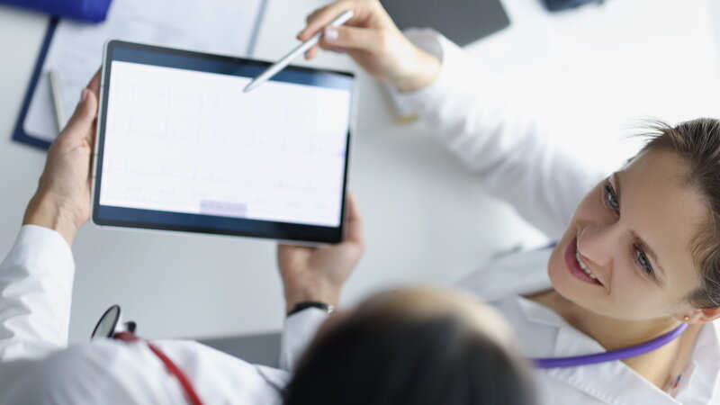 Draufsicht auf zwei Mitarbeitende im Gesundheitswesen, die Daten auf einem Tablet besprechen.