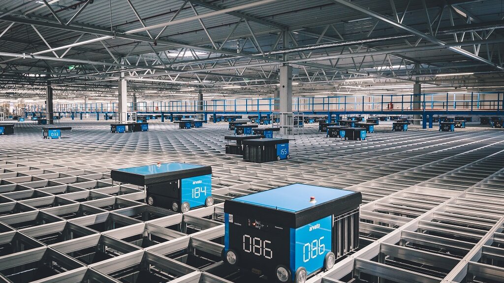Ein Innenraum einer Logistikhalle mit automatisierten Transportboxen auf einem Metallschienengitter.