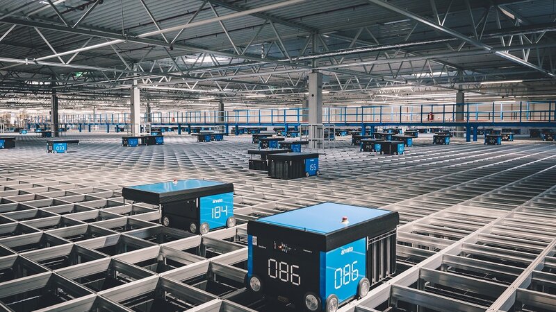 Ein Innenraum einer Logistikhalle mit automatisierten Transportboxen auf einem Metallschienengitter.
